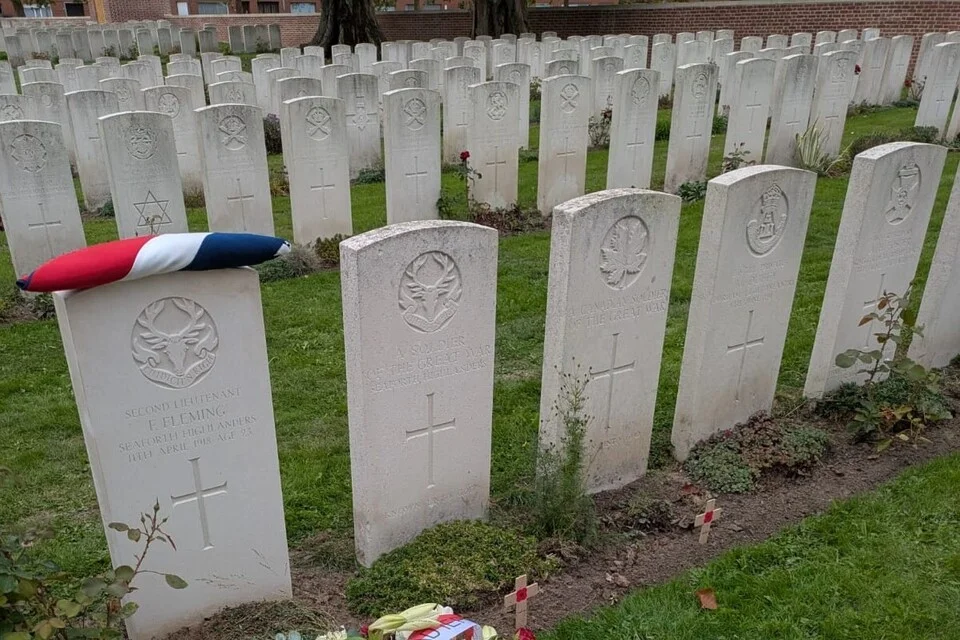 A row of white Commonwealth War Graves Commission headstones. The one on the left carries the Seaforth Highlanders badge and reads Second Lieutenant F. Fleming, Seaforth Highlanders, 11th April 1918, age 23, with a Union flag laid on top
