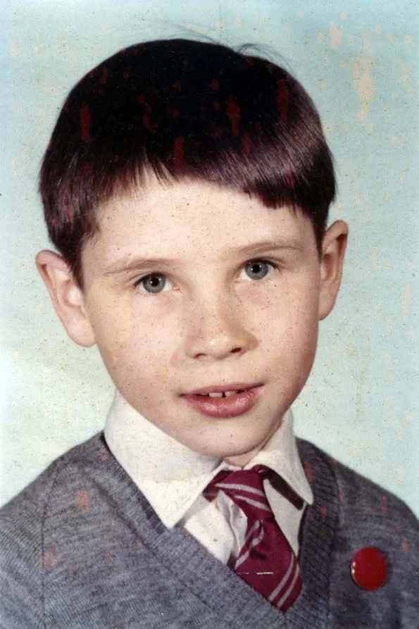 A school photograph of a boy in a grey jumper and striped tie